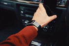 Stylish man wearing a black Apple Watch with a sleek band, reaching for a smartphone in a car, showcasing the best Apple Watch bands for men.