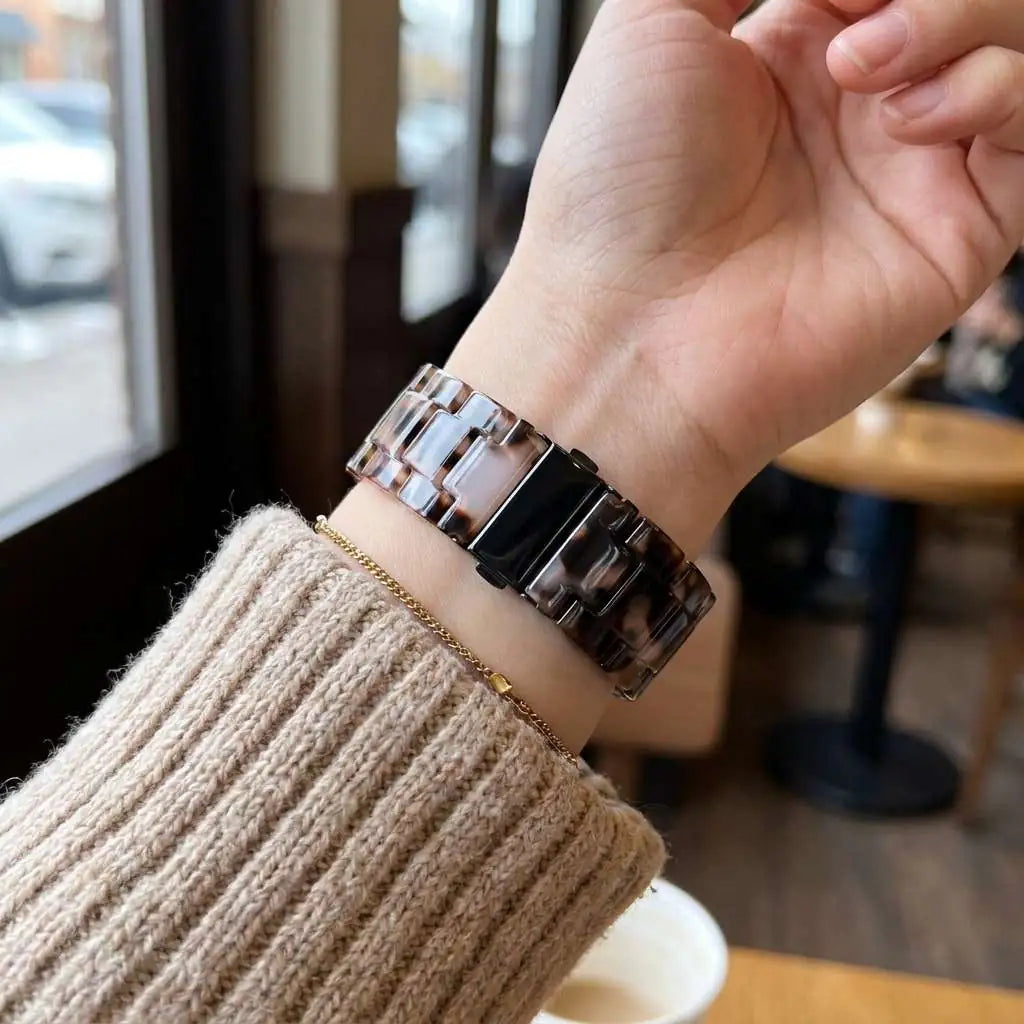 Anhem Amber Resin Apple Watch band with a translucent tortoiseshell pattern worn on a wrist with a beige sweater.