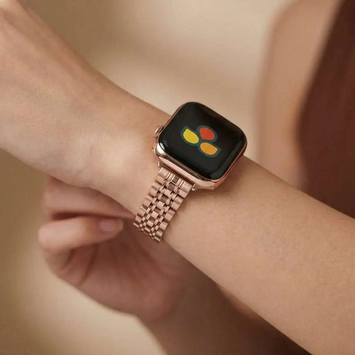 Rose gold stainless steel apple watch band on a wrist with a blurred background