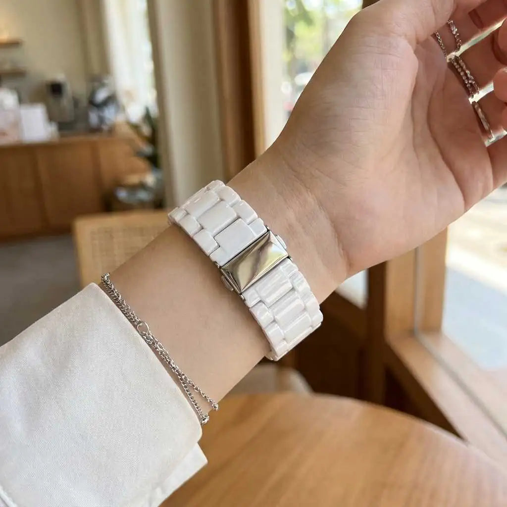 Anhem white ceramic 3-link Apple Watch band with a polished silver buckle worn on a wrist in a bright indoor setting.