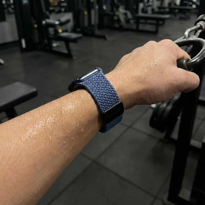 Person exercising in a gym with a blue woven apple watch on wrist